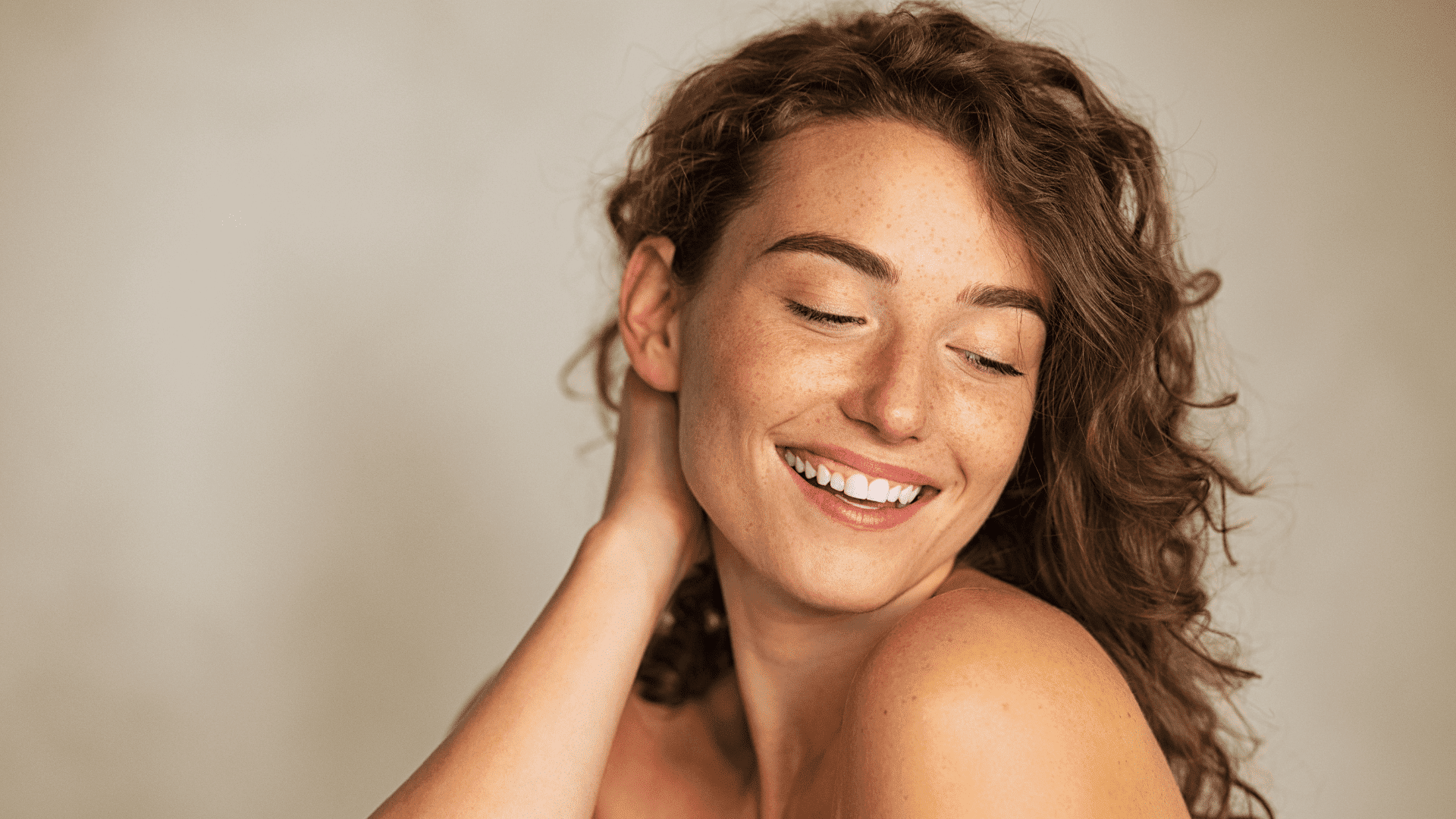 Smiling person with curly hair, looking over their shoulder against a neutral background.