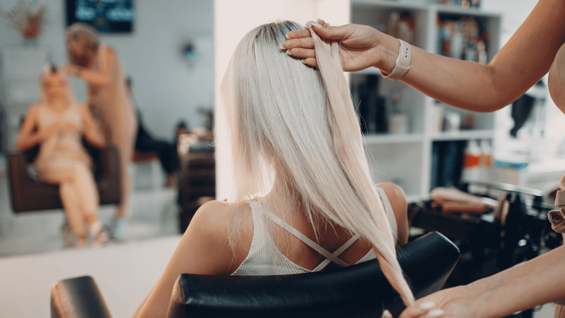 A hairstylist works on a woman's long, straight blonde hair in a salon.